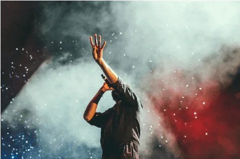 Chanteur sur scène qui chante, avec en fond des fumées bleues, blanc et rouge