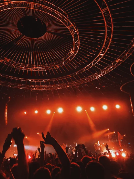 Photographie d'une foule dans un concert, lumière orangée et scène visible au loin.