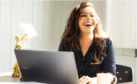 Femme rigolant devant son écran d'ordinateur, installée à son bureau
