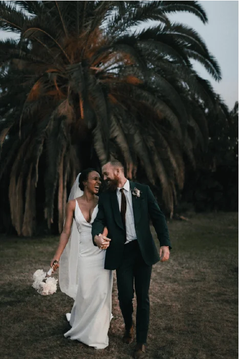 Photographie d'un couple en tenue de mariés, se souriant, devant un grand palmier.
