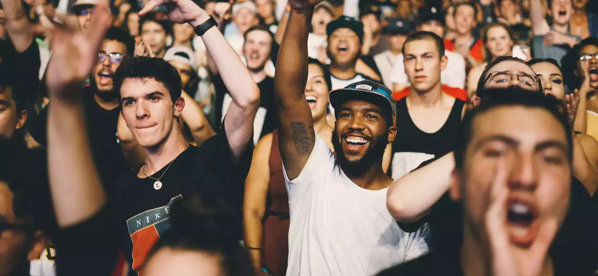 Foule dans un concert, levant les bras, souriants.